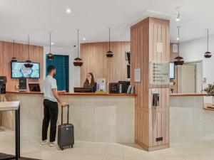 un homme avec une valise debout à un comptoir dans l'établissement Mercure Paris Porte d'Orleans, à Montrouge