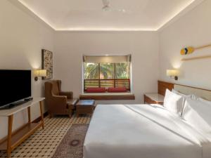 a hotel room with a large bed and a television at Novotel Goa Dona Sylvia Resort in Cavelossim