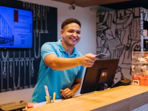 Un uomo in piedi al bancone con un cellulare in mano di ibis budget Barbacena a Barbacena