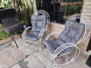 Dos sillas de mimbre blancas y una parrilla en un patio. en Hospedaje SKYHOME II, en Nu Guazu