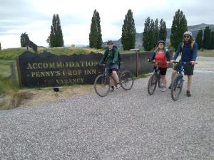 Tres personas en bicicleta delante de un cartel en Penny's Drop Inn, en Cromwell