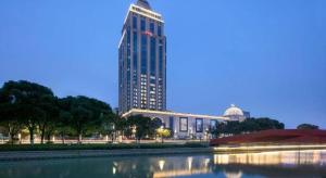 a tall building with a reflection in a body of water at Hampton by Hilton Suzhou XiangCheng in Suzhou