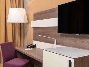 Una habitación con un escritorio con televisión y una silla. en Mercure Makkah Aziziah, en La Meca