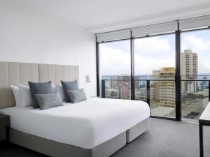 a bedroom with a large white bed and large windows at Mantra Circle On Cavill in Gold Coast