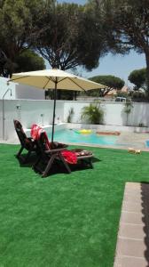2 sillas y sombrilla junto a la piscina en Chalet Merkal, en Chiclana de la Frontera