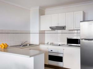 a white kitchen with a sink and a refrigerator at Mantra Esplanade in Cairns +50 photos