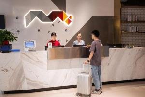 Ein Mann mit einem Koffer, der vor einer Theke steht. in der Unterkunft Borrman Hotel Baise High-speed Railway Station Hengning Plaza in Qitang