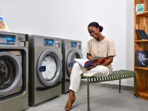 Una mujer sentada en un banco frente a una lavadora en Aparthotel Adagio Abidjan Marcory, en Abiyán