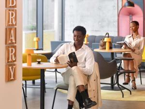 a man sitting in a chair reading a book at Aparthotel Adagio Abidjan Marcory in Abidjan