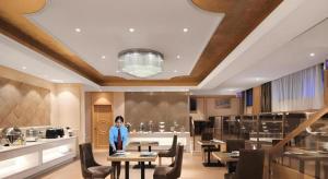 a woman standing in a restaurant with tables and chairs at Vienna Hotel Hangzhou Jiubao Sijiqing Suanli Town in Yuhang