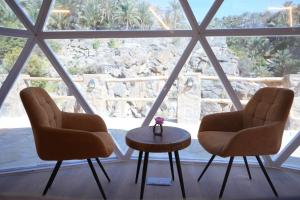 Dos sillas y una mesa frente a una ventana. en Rabwa Geodesic Dome, en Misfāh