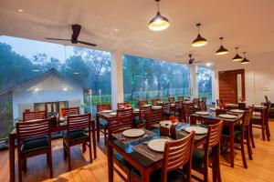 a restaurant with wooden tables and chairs and a large window at Cardamom Village Hill Resort by EGH in Thekkady
