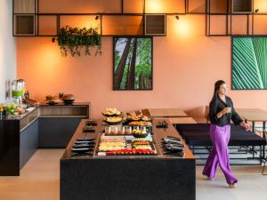 a woman standing in a kitchen with a table of food at ibis Tubarão in Tubarão