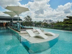 una piscina con 2 sillas blancas y una sombrilla en Gem Forest Hotel Nairobi - MGallery Collection, en Nairobi
