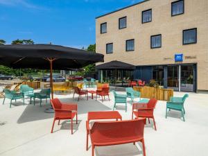 eine Terrasse mit Stühlen, Tischen und einem Sonnenschirm in der Unterkunft ibis budget Arlon Porte du Luxembourg in Arlon