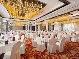 une salle de banquet avec des tables et des chaises blanches et des lustres dans l'établissement Grand Mercure Kunming South, à Kunming