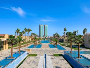 un chemin bordé de palmiers et d'un grand bâtiment dans l'établissement Rixos Obhur Jeddah Resort & Villas - All-Inclusive, à Djeddah