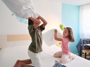 - deux enfants jouant avec des oreillers sur un lit dans l'établissement Greet Hôtel Saint-Nazaire Trignac Nouvelle Marque du Groupe Accor, à Trignac