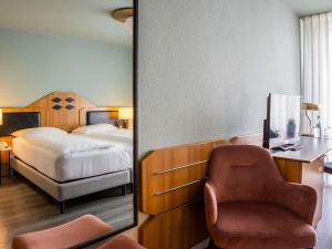 a bedroom with a bed and a chair and a mirror at Mercure Hotel Pforzheim in Pforzheim