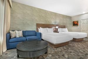 a hotel room with two beds and a blue couch at University Park Inn & Suites, an Ascend Collection Hotel in Davis +113 photos