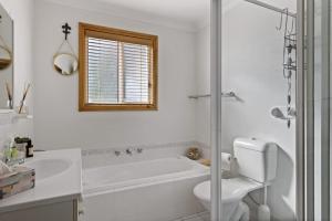 a white bathroom with a tub and a toilet at Jillby's House - 3 BR home near Narrawallee Beach in Narrawallee