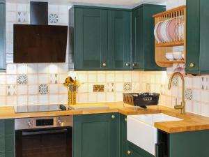 een keuken met groene kasten en een spoelbak bij The Cottage - Uk50652 in Stithians
