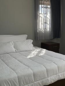 Una cama blanca en un dormitorio con ventana. en Maneph, en Chilanga