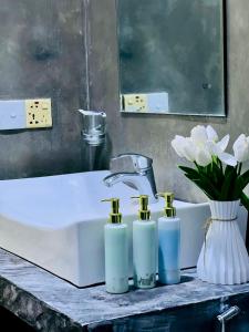 Un lavabo con tres botellas de jabón y un jarrón de flores. en 4 Axes Ella, en Ella