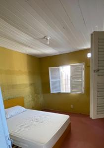 Un dormitorio con una cama blanca en una habitación amarilla. en El Gringo Banheiro Compartilhado, en Cabo de Santo Agostinho
