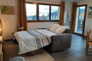 ein Schlafzimmer mit einem Bett und einer Couch und Fenstern in der Unterkunft Spacieux appartement au pied des pistes in La Feclaz