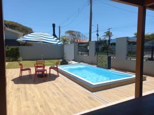 a swimming pool with two chairs and an umbrella at Casa Com Quatro Dormitórios, Pertinho Do Mar Em Capão Da Canoa in Capão da Canoa