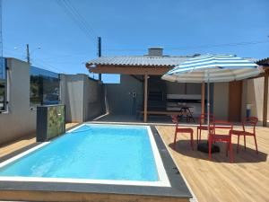 a swimming pool with an umbrella and two chairs and a table with an umbrella at Casa Com Quatro Dormitórios, Pertinho Do Mar Em Capão Da Canoa in Capão da Canoa