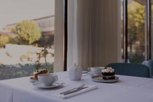 Ein Tisch mit zwei Tassen und Kuchen auf Tellern. in der Unterkunft Stella Braga Aparthotel in Braga + 22 Fotos