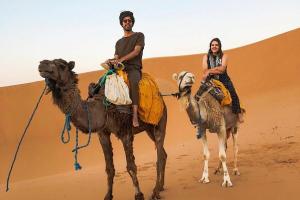 un hombre y una mujer montados en camellos en el desierto en Merzouga Best Luxury Camp, en Merzouga