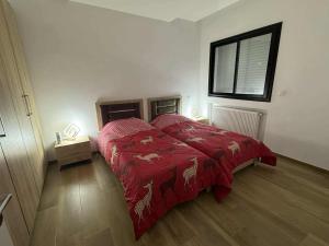a bedroom with a bed with a red comforter and a window at New Sweet Home Soukra in Sukrah
