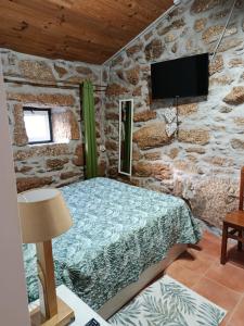 ein Schlafzimmer mit einem Bett und einem TV an einer Steinmauer in der Unterkunft Quintinha das Artes - Turismo Rural in Pinhel