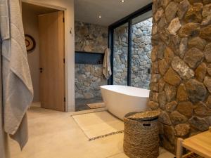 Izakithi River Villa في ماليلين: حمام مع حوض استحمام وجدار حجري