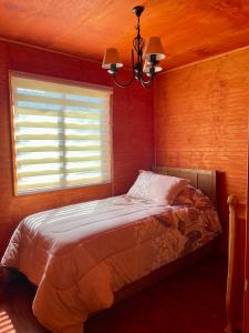 a bedroom with a bed with a window and a chandelier at Cabaña Canelita in Cochrane