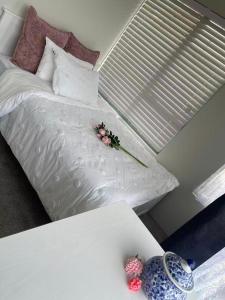 a white bed with flowers on it with a table at 2 Bedroom Cozy Space Near Botany in Auckland +3 photos