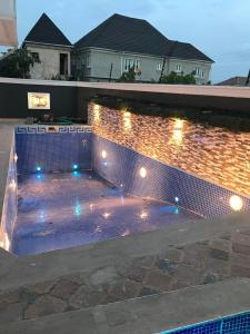 - une piscine avec des lumières sur un mur en briques dans l'établissement AlphaDreams Villa, à Magodo