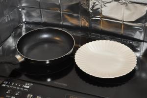 Una sartén sobre una estufa con una pila de platos de papel en GOOSESTAY Koza, en Okinawa City