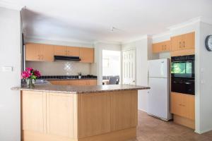 Una cocina con gabinetes de madera y un refrigerador blanco. en Leafy Retreat - spacious holiday home near harbour, en Ulladulla