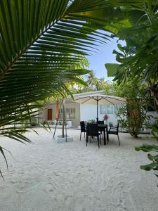 einen Tisch und Stühle unter einem Sonnenschirm am Strand in der Unterkunft The Palm Retreat Maldives in Gaafaru