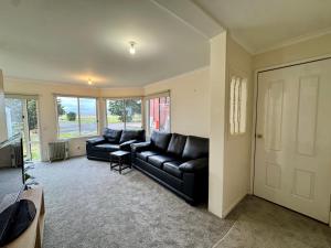 a living room with black leather couches and a television at Private Farmhouse & Paddock Available in Werribee South +9 photos
