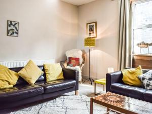 een woonkamer met een zwarte leren bank en gele kussens bij Maisie Cottage in Saint Monance