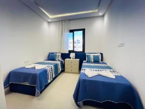 two beds in a room with blue and white sheets at Colina Smir par Immo Marina Vacances de Rêve C1-10 in Oulad Akkou +5 photos