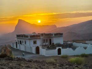 a house in the desert with the sunset in the background at Jabal Shams bayt kawakib in Misfāh