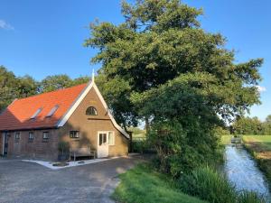 un bâtiment avec un toit orange à côté d'une rivière dans l'établissement Boerderijhuisje 22 - Landelijk logeren bij Sneek, à Loënga