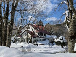 a snow covered yard with a house and trees at ペンションあけまの森 in Daisen