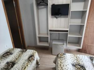a room with two beds and a tv and shelves at Hotel Vitória - Guaíra in Guaíra